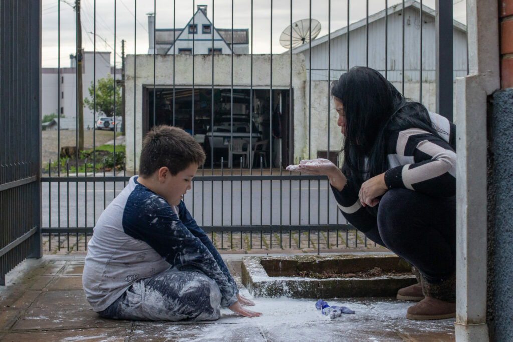 João Otávio (izquierda) y su madre Juliana Pedroso juegan juntos con un globo reventado lleno de harina de maíz en su casa en Vacaria. Pedroso sospecha que los pesticidas son la causa del síndrome neurodegenerativo extremadamente raro que le diagnosticaron al su hijo de 7 años. Créditos Anna Ortega