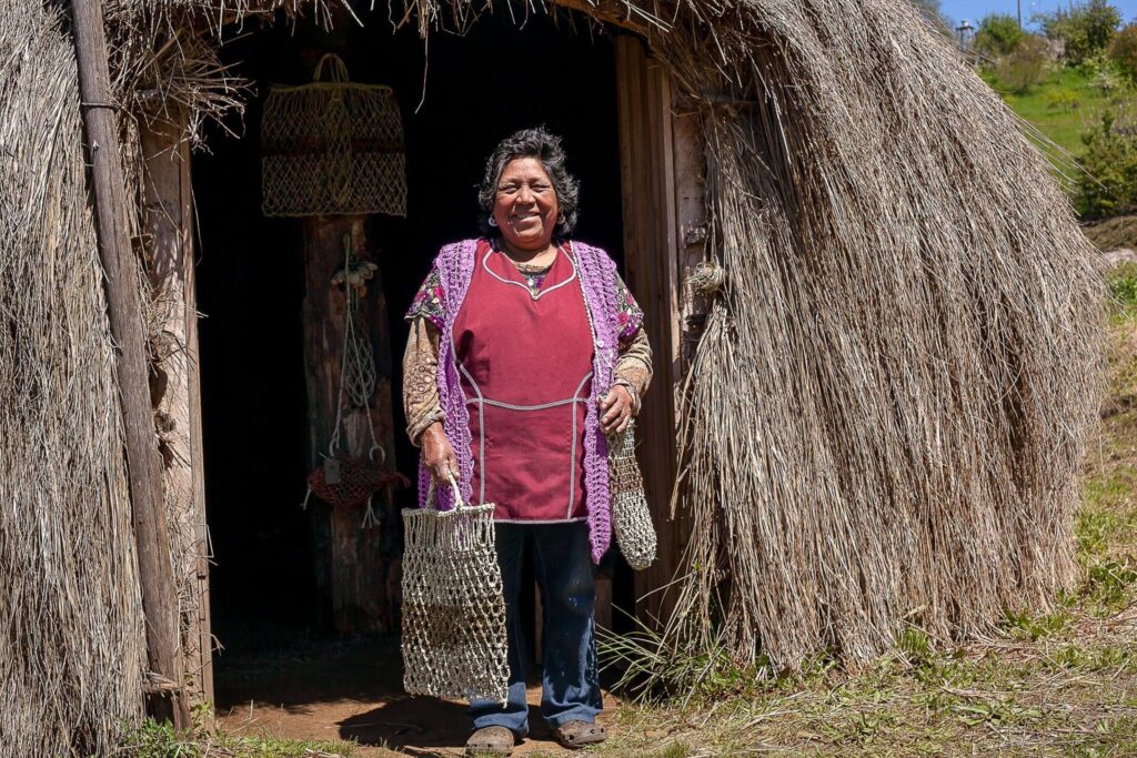 La artesana Elena Paillafil de Puerto Saavedra, mantiene el oficio del trabajo con fibra vegetal de Chupón, el cual le fue transmitido por sus ancestros y hoy cultiva junto a sus hijas. Imagen de la exhibición "Wallmapu: creadores por excelencia", del Programa de Artesanía de la Universidad Católica de Temuco. 