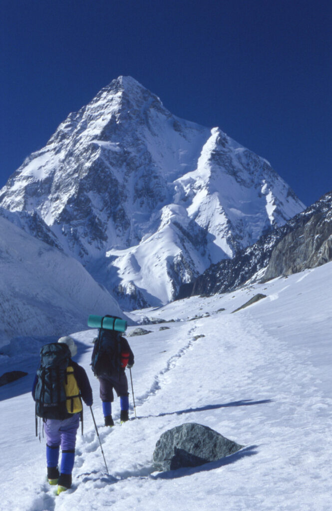 Registro al comienzo de la excursión hacia el K2, desde Concordia a 5.000 metros aproximadamente, con el campamento base al fondo del valle a 5.400 metros. En la fotografía, vemos a Marcelo Grifferos atrás acompañado por alguien más del equipo. “Esta foto es interesante y me gusta mucho, es muy bonita porque se ve el K2 completo cuando estábamos llegando. La foto muestra dos aristas, una con sol a la izquierda y otra con sombra a la derecha, una grande hacia más o menos la izquierda de la fotografía, y una un poco más chica hacia más o menos la derecha de la fotografía, y se ve muy bien nuestra ruta. Esa fue la primera ascensión integral de esa arista”, Rodrigo Jordán. Créditos: Vertical